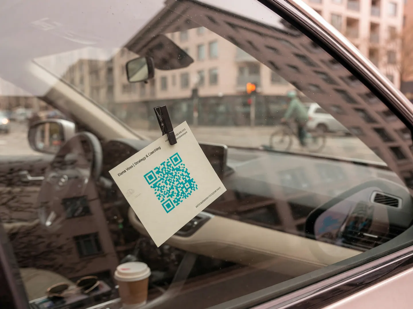 A small contact card with a QR code clipped inside a car windscreen, seen from the street.