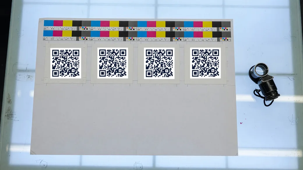 A press proof sheet on a light table with printed QR codes and colour bars.