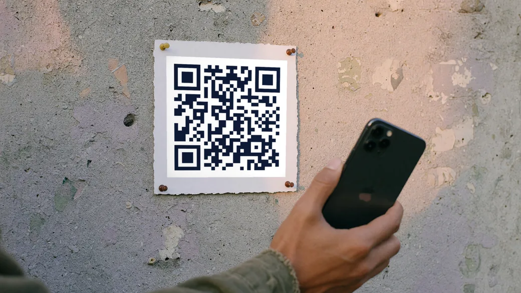 A phone held up to a printed QR code on a wall poster, the code filling the camera view.